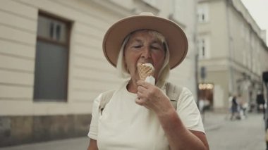 Yaşlı bir kadın şehirde dolaşırken dondurma külahı yiyor. Güneşli bir günde tatlı bir ziyafetin tadını çıkarıyor. Şapka ve rahat giysiler giyiyor..