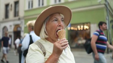 Yaşlı bir kadın şehirde dolaşırken dondurma külahı yiyor. Güneşli bir günde tatlı bir ziyafetin tadını çıkarıyor. Şapka ve rahat giysiler giyiyor..