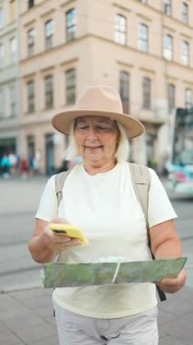 Yaşlı bir kadın güzel bir şehir meydanında elinde haritayla manzaranın tadını çıkarıyor. O rahat bir kıyafet giyer, şapka ve güneş gözlüğü takar..