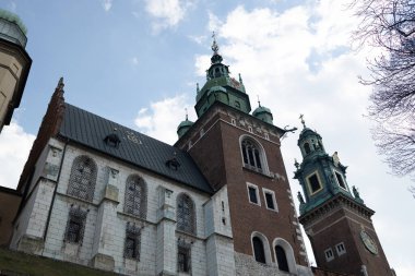 Polonya 'nın Krakow kentindeki tarihi katedral binasında yüksek kuleler ve karmaşık mimari yapılar yer alıyor. Fotoğraf, kilisenin ihtişamını ve güzelliğini vurgulayan açık mavi bir gökyüzüne karşı çekilmiştir.