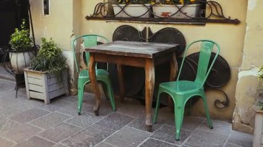 Ahşap bir masası ve kaldırıma kurulmuş iki adet yeşil metal koltuğu olan rahat bir açık kafe. Büyüleyici şehir sahnesinde pencere kenarında dekoratif bitkiler var.