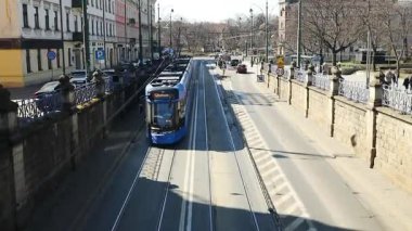 Krakow, Polonya sokaklarında mavi tramvay gezintisi, şehrin verimli toplu taşıma sistemini gözler önüne seriyor. İkonik tramvay tarihi şehirde tanıdık bir manzara, kentsel bir bakış sunuyor.