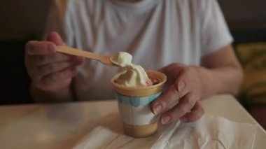 Son sınıf öğrencisi bir kafede elinde tahta kaşıkla bir fincan dondurmanın keyfini çıkarırken, çevre dostu tüketim uygulamalarını ön plana çıkarıyor. Görüntü sürdürülebilirliği ve biyolojik olarak bozunabilir maddelerin kullanımını teşvik eder.