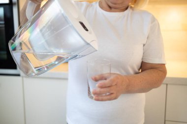 Mutfakta elinde bir sürahi ve bir bardak tutan mutlu bir son sınıf öğrencisi, kendine ferahlatıcı bir içki koymaya hazır. Bu görüntü evdeki sağlıklı alışkanlıkları ve keyifli anları yansıtıyor.