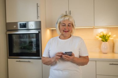 Son sınıf öğrencisi bir kadın mutfağında duruyor, gülümsüyor ve en sevdiği müziğin tadını çıkarıyor. Telefonundan melodileri dinliyor, rahat evindeki o anın mutluluğunu kucaklıyor.