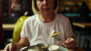 Bıçak ve çatal tutan kişi, yanında ekşi krema ve küçük bir tabakla servis edilen geleneksel hamur köftelerini yemeye hazır. Sahne rahat bir restoranda, nefis şeyler sergiliyor.