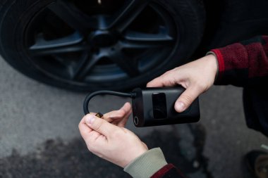 Adam sürücü elinde araç lastikleri şişiriyor, hava basıncını kontrol etmek ve benzin istasyonunda tekerleği doldurmak için lastik kapakçığı kapağını çıkarıyor. Kişisel hizmet, bakım ve güvenlik. Yüksek kalite