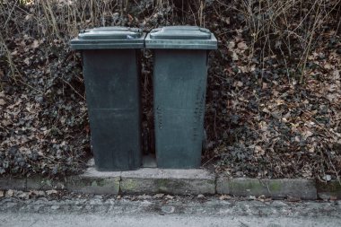 Sokakta bir evin yakınına konmuş iki siyah çöp kutusu tipik bir şehir manzarası yaratıyor. Bir yerleşim bölgesinde günlük yaşam ve atık yönetimini gösteren basit ama pratik bir görüntü.