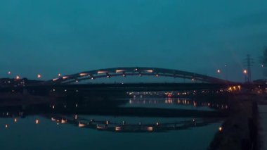 Polonya 'nın Krakow kentindeki Vistula Nehri üzerindeki Bernatka Footbridge' in sakin bir akşam görüntüsü. Sokak lambaları suyu yansıtıyor ve alacakaranlıkta huzurlu bir şehir atmosferi yaratıyor..