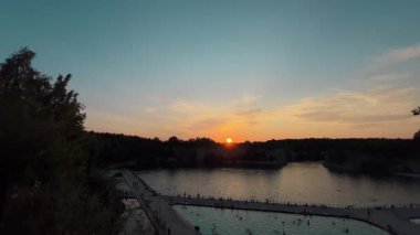 Polonya, Krakow yakınlarında huzurlu bir gölün üzerinde güzel bir günbatımı. İnsanlar dinlenmek ve manzaranın tadını çıkarmak için deniz kenarında toplanıyor. Sıcak ve dingin bir yaz akşamı sahnesi yaratıyorlar..