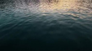 Yumuşak su dalgalarının yakın çekimi günbatımının yumuşak renklerini yansıtıyor, muhtemelen Polonya 'nın Krakow yakınlarındaki bir göl ya da nehirde. Huzurlu doğa dokusu arka plan ve barışçıl görsel temalar için mükemmeldir..