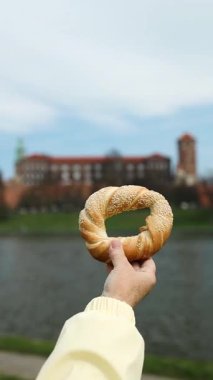 Geleneksel bir Krakow simit obwarzanek 'i tarihi Wawel Kalesi ve Vistula Nehri' nin arka planına karşı tutarak. Polonya 'da yerel yiyecek, kültür ve seyahatin mükemmel bir kombinasyonu.