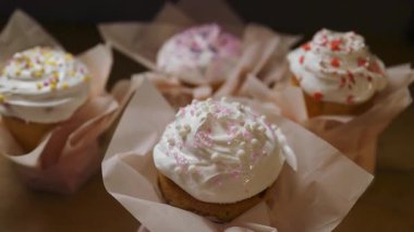 Beyaz krema ve renkli şeker parçacıklarıyla süslenmiş bir grup neşeli kek. Pastel kağıda sarılmış bu ev yapımı tatlılar Paskalya, bahar tatilleri ve tatlı mutfak malzemeleri için mükemmeldir..