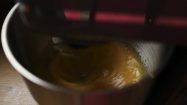 Tahta bir yüzeyde metal bir kasede yumurta ve şeker çırpan bir elektrikli standın yakın çekimi. Ev yapımı konusunda ayrıntılı bir adım, yemek dersleri, tarif içeriği ve yemek blogları için ideal.