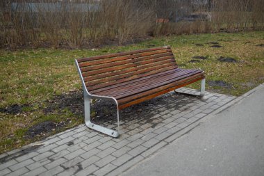 Yürüyüş yolu boyunca ahşap bir bankın olduğu huzurlu bir park sahnesi. Kamu parkındaki ağaçların ve yeşilliğin tadını çıkarırken bank dinlenmek için bir yer sağlıyor.