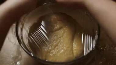 Dinlenmesi ve yükselmesi için plastik ambalajla kaplanmış cam bir kasedeki zengin maya hamurunun tepeden tırnağa görüntüsü. Klasik bir pişirme adımı, özel dersler, ev yemekleri ve zanaatkar mutfak içeriği için mükemmel..
