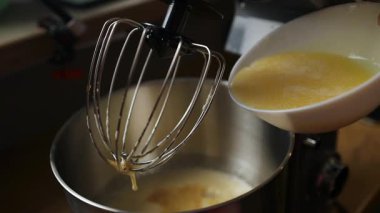 Sıvı karışımın yakın plan görüntüsü, muhtemelen tereyağı ve yumurta çırpma kabıyla karıştırma kabına dökülüyor. Tatlı ya da ekmek pişirmede anahtar bir an, yemek tarifleri ve yemek dersleri için mükemmel.