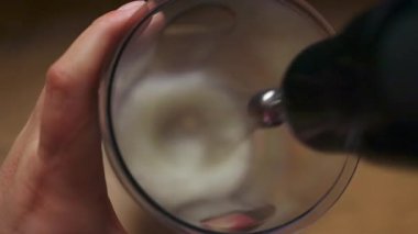 Sütün el yapımı elektrikli çırpı kullanılarak bir bardakta köpürtüldüğü yakın plan görüntüsü. Kahve tarifleri, kahvaltı ritüelleri ve yemek videoları için mükemmel dinamik bir aşçılık sahnesi..