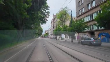 Krakow, Polonya 'daki yeşil şehir caddesinde tramvay rayları. Krakow 'da yapraklı bir caddede, tramvay rayları boyunca ilerleyen yüksek kaliteli 4K' lık bir görüntü. Konut binaları, ağaçlar ve şehir manzarası.