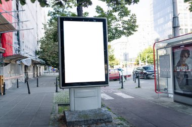 Otobüs durağının yanındaki kaldırımda, binalar, arabalar ve ağaçlar gibi kentsel unsurlarla çevrili boş bir şehir afişi. Reklamlar, anonslar ya da görseller eklemek için ideal