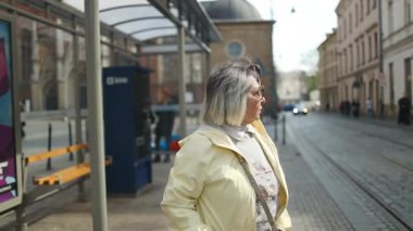 Polonya 'nın Krakow kentinde toplu taşımayı beklerken bir tren durağında durup etrafa bakınan yaşlı bir kadın. Yaşlılar için hareketlilik, bağımsızlık ve şehir yaşamını vurgulayan şehir seyahati sahnesi.
