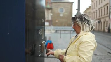 Polonya 'nın Krakow kentindeki bir şehir caddesinde otomattan tramvay bileti alan yaşlı bir kadın. Bağımsızlığı, toplu taşımayı ve günlük seyahat rutinlerini vurgulayan modern bir kentsel an.