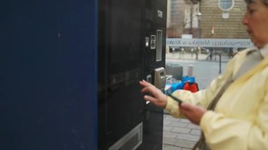 Polonya 'nın Krakow kentindeki bir şehir caddesinde otomattan tramvay bileti alan yaşlı bir kadın. Bağımsızlığı, toplu taşımayı ve günlük seyahat rutinlerini vurgulayan modern bir kentsel an.