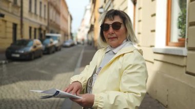 Elinde harita olan gülümseyen yaşlı kadın, Polonya 'nın Krakow kentinin büyüleyici eski sokaklarını keşfederken uzaktaki bir yeri işaret ediyor. Etkin kıdemliyi vurgulayan neşeli ve bağımsız bir seyahat anı