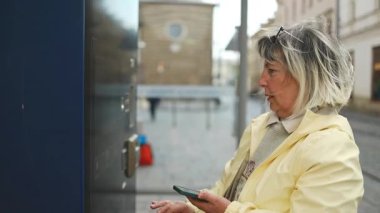Polonya 'nın Krakow kentindeki bir şehir caddesinde otomattan tramvay bileti alan yaşlı bir kadın. Bağımsızlığı, toplu taşımayı ve günlük seyahat rutinlerini vurgulayan modern bir kentsel an.