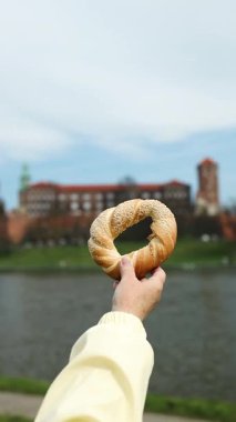 Geleneksel bir Krakow simit obwarzanek 'i tarihi Wawel Kalesi ve Vistula Nehri' nin arka planına karşı tutarak. Polonya 'da yerel yiyecek, kültür ve seyahatin mükemmel bir kombinasyonu.