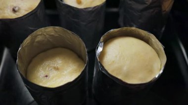 Çiğ Paskalya ekmeği ya da kek hamuru siyah silindirik şekillerde pişirilmeye hazır. Geleneksel pişirme, yemek blogları, tarifler ve mevsimsel mutfak içeriği için ideal bir hazırlık aşaması.