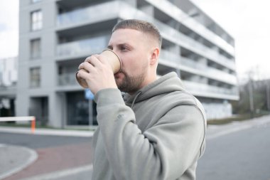 Kahve içen yakışıklı genç adam. Elinde kağıt kahve fincanı tutan sakallı bir adam şehir caddesinde yürüyor.