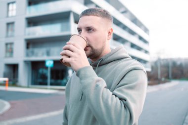 Kahve içen yakışıklı genç adam. Elinde kağıt kahve fincanı tutan sakallı bir adam şehir caddesinde yürüyor.