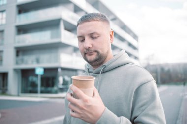 Kahve içen yakışıklı genç adam. Elinde kağıt kahve fincanı tutan sakallı bir adam şehir caddesinde yürüyor.