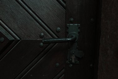 Siyah işlemeli demir saplı, köşegen şeklinde desenli tahtaları olan koyu ahşap bir kapının detaylı görüntüsü. Görüntü, kalıtım, işçilik ve eski dünyanın mimarisini gösteriyor.