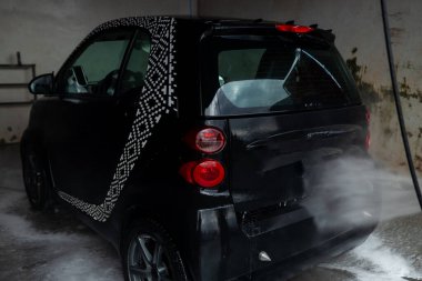 Kadın arabasını oto yıkama istasyonunda yıkıyor. Araba yıkama servisi. Oto yıkamada siyah arabaya köpük süren bir adam.