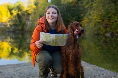 Mutlu kadın köpekle seyahat ediyor. Gölün kenarında oturan güzel bir kadın ve İrlandalı Setter köpeği etrafa bakınıyorlar. Mutlu kız, dağ ve orman manzarası ile yürüyüş yaparken evcil hayvanıyla etkileşime girer..