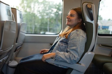 Gülümseyen bir kadın modern bir Polonya treninde pencerenin kenarında oturmuş yolculuğunun tadını çıkarıyor. Sıcak ve rahat bir seyahat sahnesi turizm, yaşam tarzı ve ulaşım için idealdir..