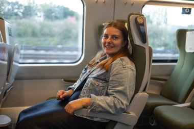 Gülümseyen bir kadın modern bir Polonya treninde pencerenin kenarında oturmuş yolculuğunun tadını çıkarıyor. Sıcak ve rahat bir seyahat sahnesi turizm, yaşam tarzı ve ulaşım için idealdir..
