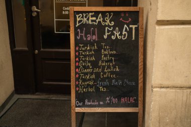 Bir kafe önünde ahşap çerçeveli karatahta, Türk çayı, omlet ve bitki çayı gibi şeylerin listelendiği el yazısıyla yazılmış bir kahvaltı menüsü sergiliyor. Samimi sunum yoldan geçenleri güne başlamaya davet ediyor