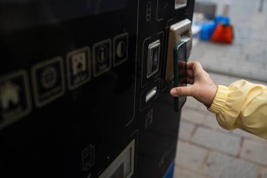 Krakow 'daki bilet makinesine ödeme yapmak için telefon ya da telefon kullanan bir kadının yakın çekimi. Sokak sahnesi Polonya 'daki modern şehir geçişini yansıtıyor.