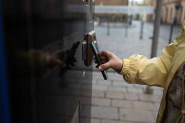 Krakow 'daki bilet makinesine ödeme yapmak için telefon ya da telefon kullanan bir kadının yakın çekimi. Sokak sahnesi Polonya 'daki modern şehir geçişini yansıtıyor.