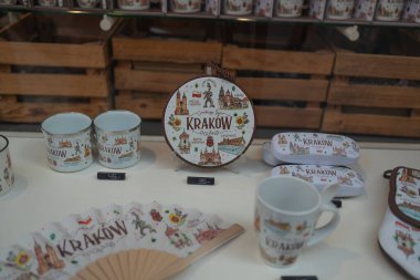 KRAKOW, POLAND -2 Nisan 2025: Krakow hediyelik eşya dükkanının vitrininde sembolik Polonya sembolleri ve şehir simgeleri ile süslenmiş temalı seramik bardaklar, tabaklar, kalem kılıfları ve yelpazeler sergileniyor. Samimi bir vitrin.