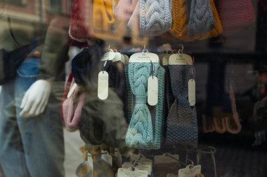 Krakow 'daki bir mağaza vitrininde şapka ve fular da dahil olmak üzere renkli kış aksesuarları sergileniyor. Tarihi binaların yansımaları ve ceketli bir manken rahat sokak sahnesine derinlik katıyor..