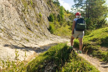 Sırt çantalı ve kırmızı şapkalı yaşlı bir kadının dağ vadisinde dar kayalık bir patikada yürüdüğünü gördüm. Yeşillik ve sarp kayalıklarla çevrili bu sahne özgürlüğü, gücü ve...
