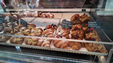 Çikolata, meyve ve krema dolu seçenekler de dahil olmak üzere çeşitli lezzetli kruvasan ve hamur işleriyle dolu bir fırın vitrininin yakın görüntüsü. Cam tezgahlar taze pişmiş olanları gösteriyor.