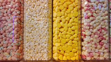 Renkli şekerlerin dört dikey şeffaf konteynırda düzgün sıralanmış yakın görüntüsü. Tatlılar arasında pembe, sarı, beyaz ve karışık pastel renkler, canlı ve davetkar bir görsel yaratıyor.