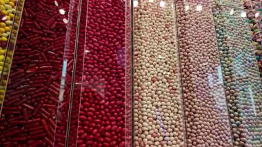 Renkli şekerlemelerden oluşan canlı bir çeşitlilik şeffaf dikey tüplerle düzenlenmiş şeker dükkanının içinde bir duvar ekranında. Görüntü, kırmızı da dahil olmak üzere çeşitli doku ve renkleri sergiliyor.