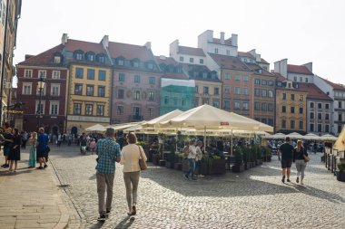 Varşova, Polonya: 3 Eylül 2023 Varşova Eski Kasabası pazar meydanında yürüyen turistler, arka planda şemsiyelerin altında kafeler ve renkli tarihi binalarla.