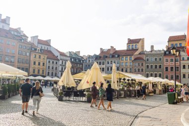 Varşova, Polonya: 3 Eylül 2023 Varşova Eski Kasabası pazar meydanında yürüyen turistler, arka planda şemsiyelerin altında kafeler ve renkli tarihi binalarla.